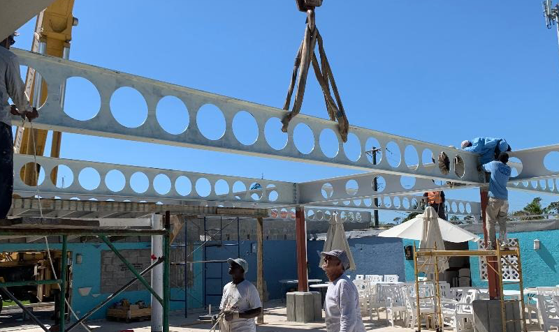 Workers use a crane to lift perforated metal beams at a construction site.