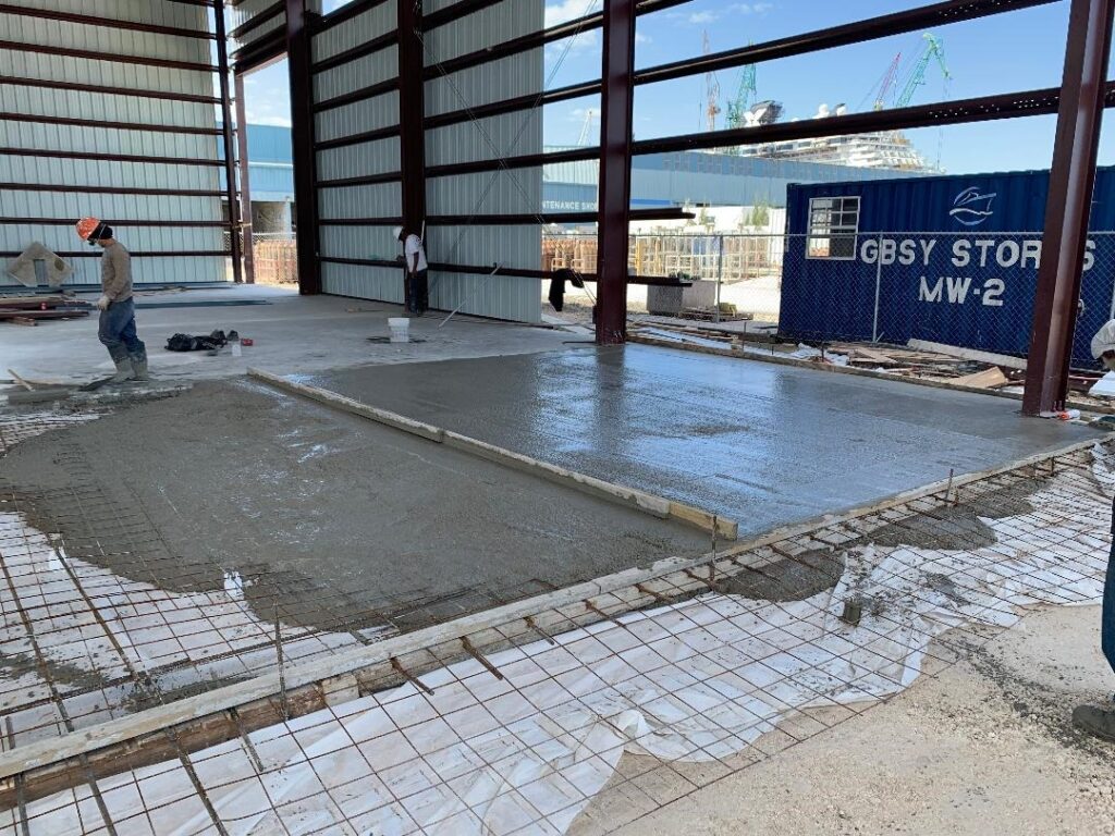 Fresh concrete being poured and leveled on a construction site floor.